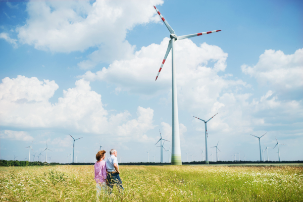 A senior couple walking on field on wind farm. Copy space.