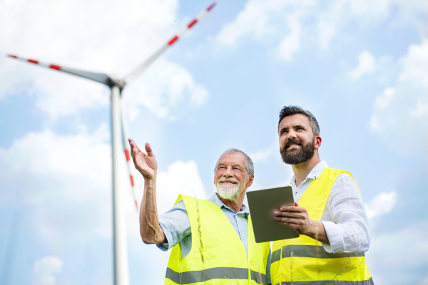 Two engineers or technicians with clipboard standing on wind farm, making notes.