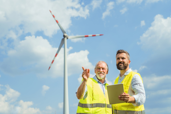 Two engineers or technicians with clipboard standing on wind farm, making notes.