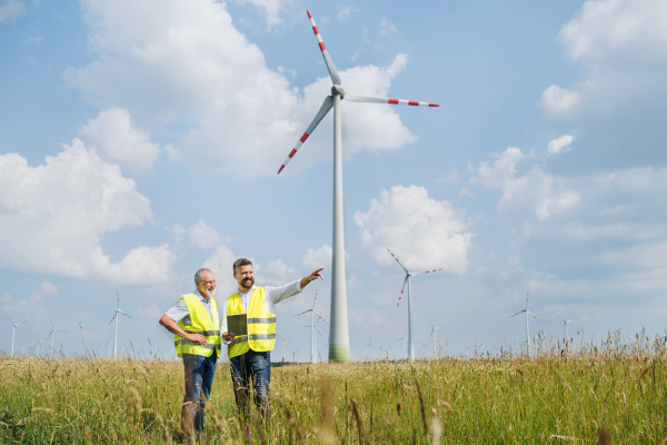 Two engineers or technicians with clipboard standing on wind farm, making notes.