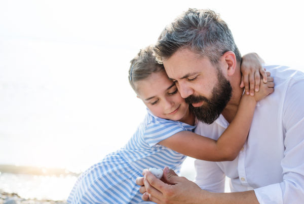 Side view of father and small daughter on a holiday sitting by the lake or sea.