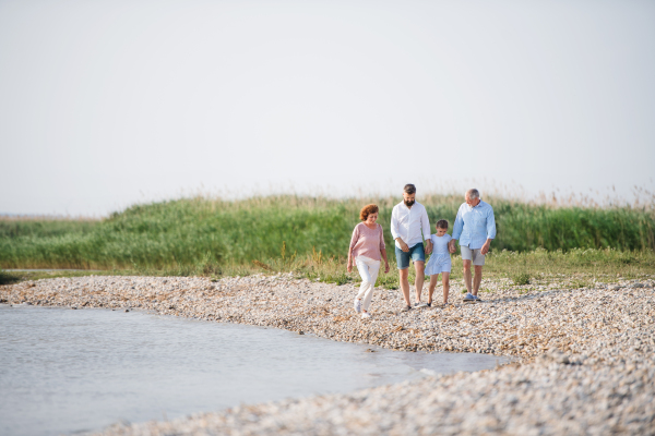 A multigeneration family on a holiday walking by the lake, holding hands.