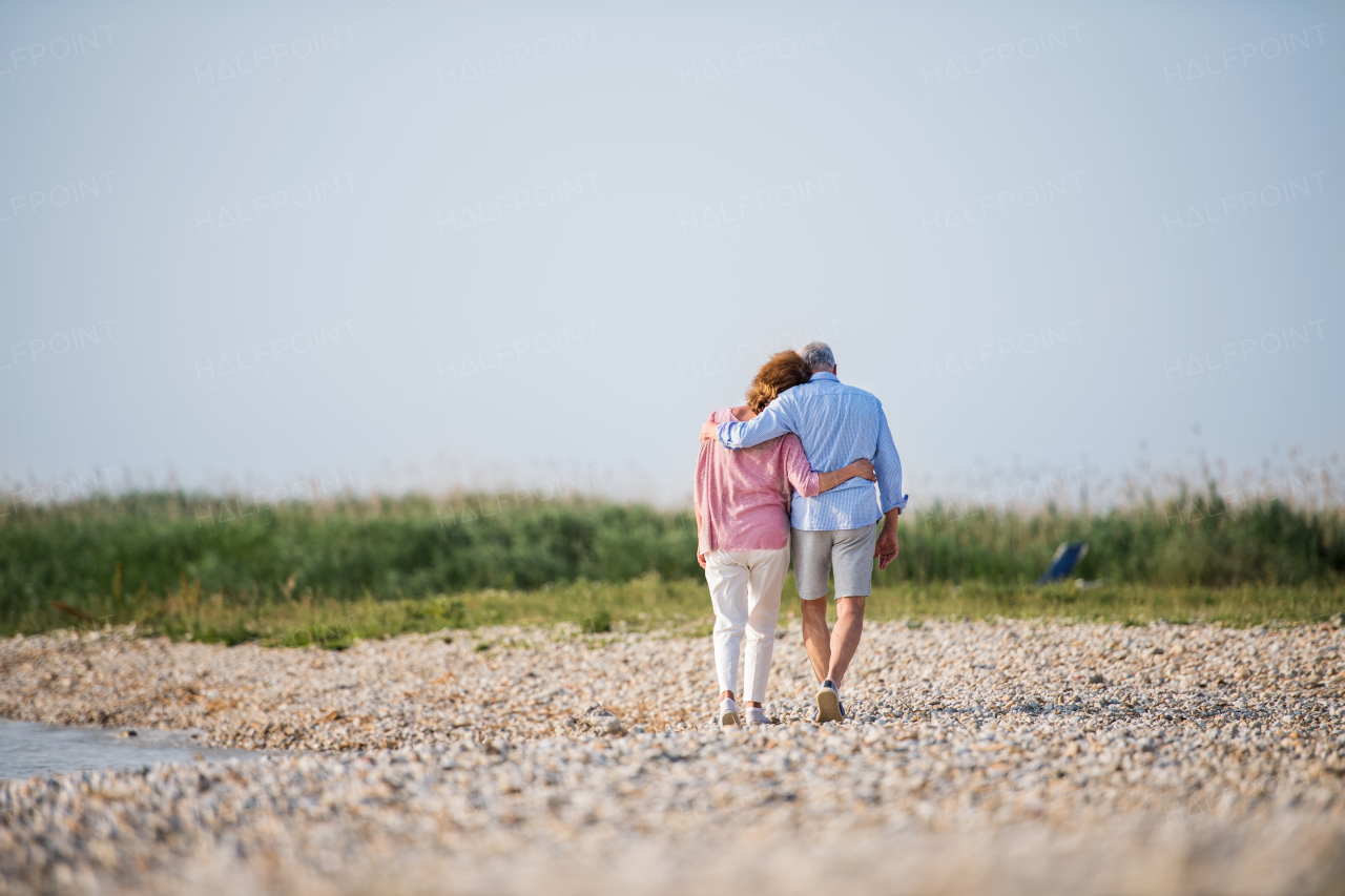 Rear view of senior couple on a holiday on a walk by the lake, walking arm in arm.