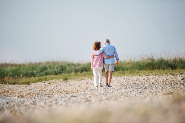 Rear view of senior couple on a holiday on a walk by the lake, walking arm in arm.