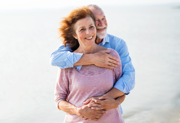 Front view of senior couple on a holiday on a walk by the lake, hugging.