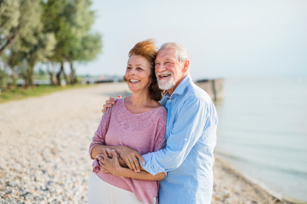 Front view of senior couple on a holiday on a walk by the lake, hugging.