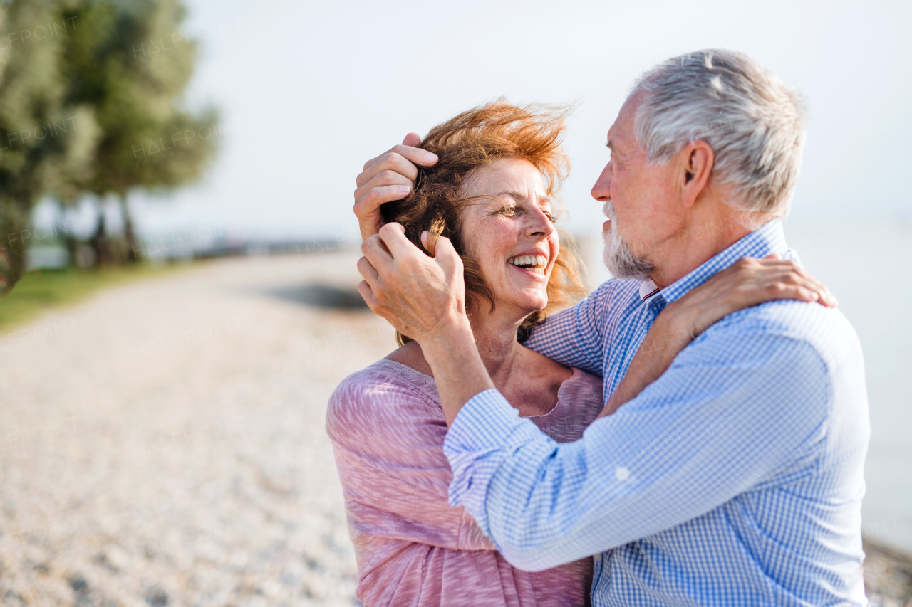 Front view of senior couple on a holiday on a walk by the lake, hugging.