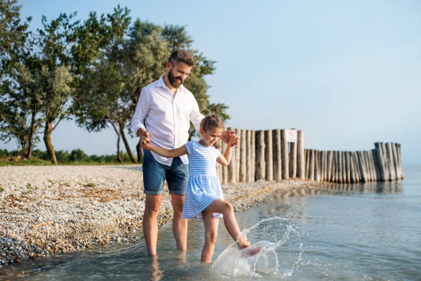 A mature father and small daughter on a holiday playing by the lake or sea, walking barefoot.