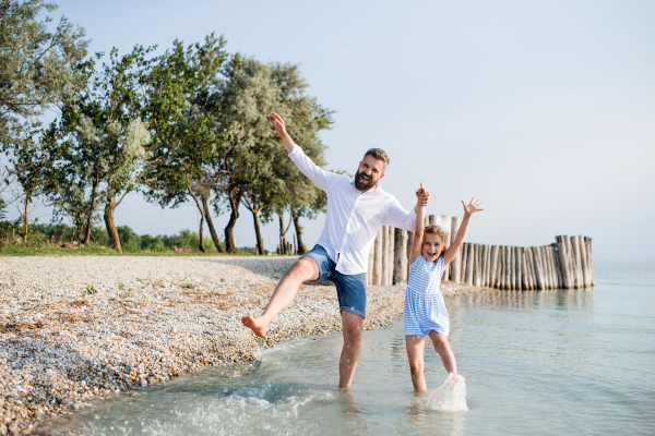 A mature father and small daughter on a holiday playing by the lake or sea, walking barefoot.