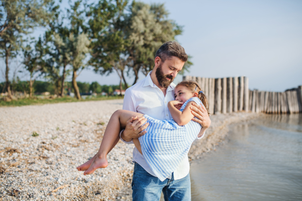 A mature father carrying small daughter on a holiday by the lake, walking.