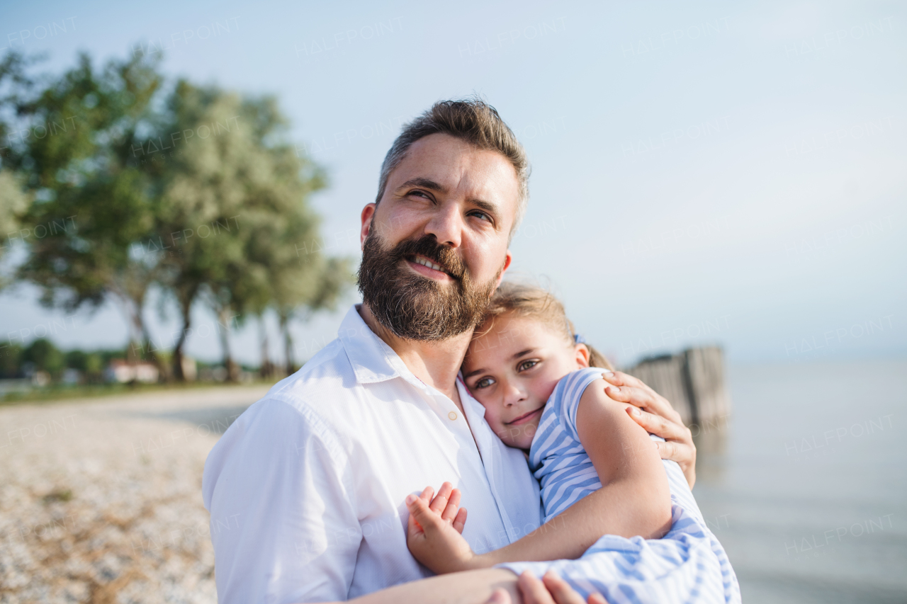 Side view of father and small daughter on a holiday sitting by the lake or sea.