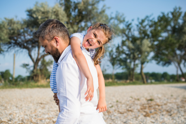 A mature father carrying small daughter on a holiday by the lake, walking.