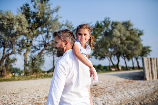 A mature father carrying small daughter on a holiday by the lake, walking.