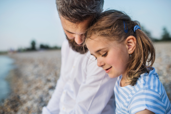 Side view of father and small daughter on a holiday sitting by the lake or sea.