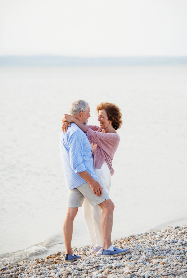 A senior couple on a holiday on a walk by the lake, hugging.