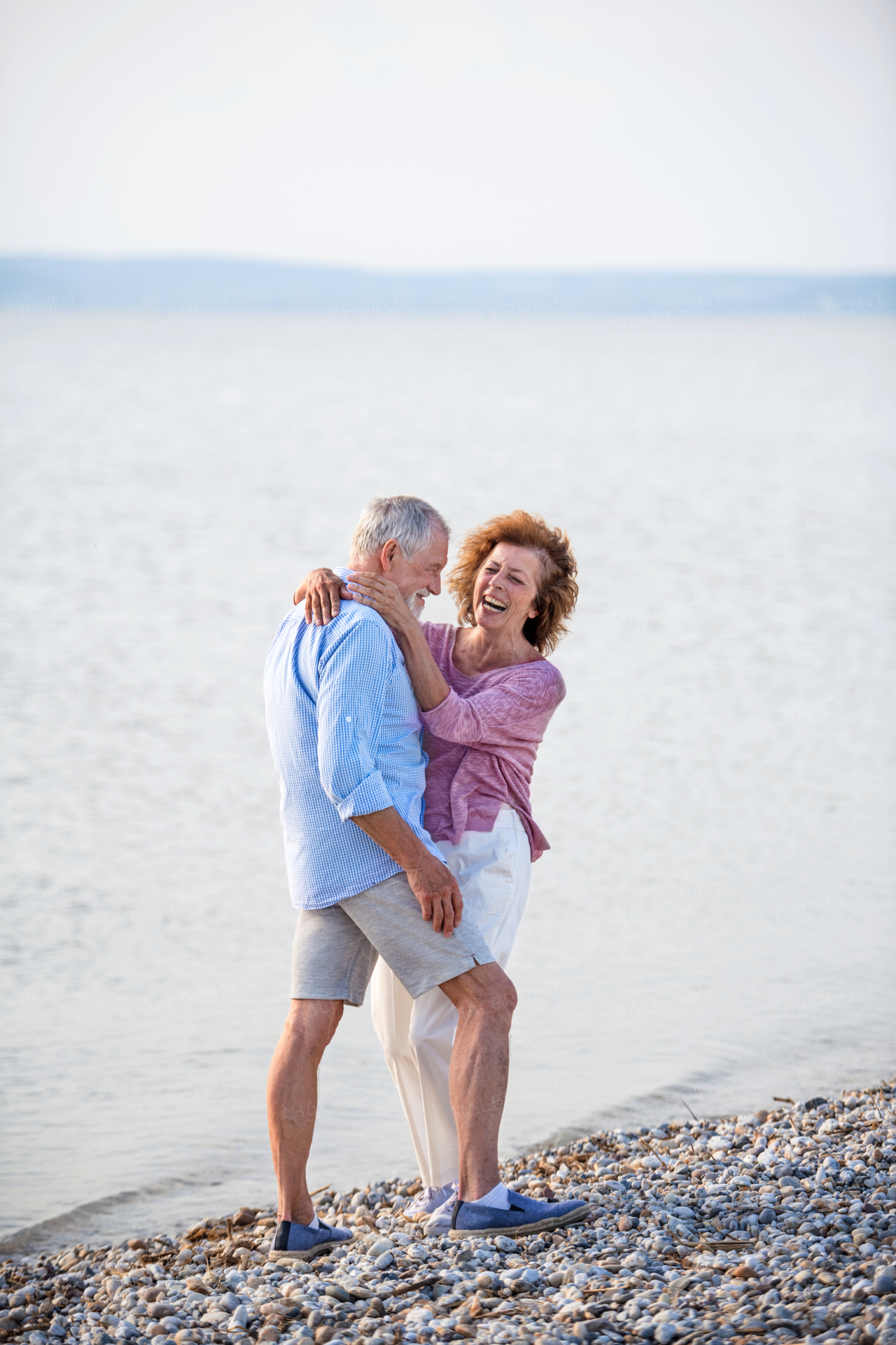 Front view of senior couple on a holiday on a walk by the lake, hugging.