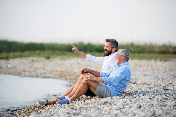 Senior father and mature son sitting by the lake, talking. Copy space.