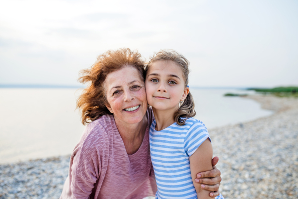 A small girl with grandmother on a holiday by the lake, looking at camera.