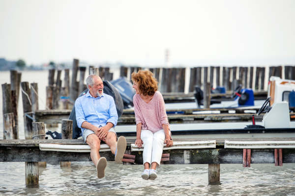 Senior couple in love on a holiday sitting by the lake, talking.