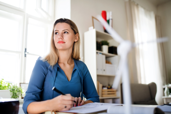 Young woman architect sitting at the desk indoors in home office, working.