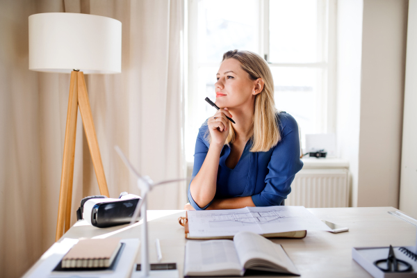 Young woman architect sitting at the desk indoors in home office, working.