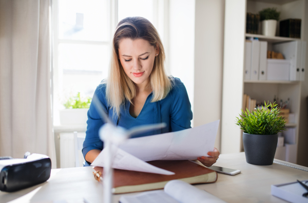 Young woman architect sitting at the desk indoors in home office, working.