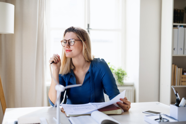 A young woman architect sitting at the desk indoors in home office, working.