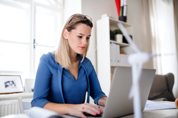 Young woman architect with laptop sitting at the desk indoors in home office, working.