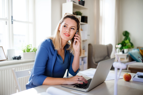 A young woman architect with smartphone sitting at the desk indoors in home office, working.