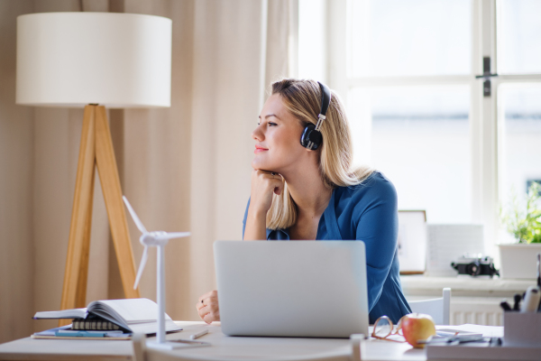 A young woman engineer with headphones sitting at the desk indoors in home office.