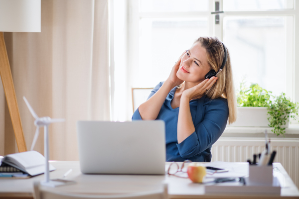 Young woman with laptop and headphones sitting at the desk indoors in home office.