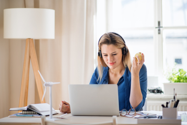 A young woman engineer with headphones sitting at the desk indoors in home office.