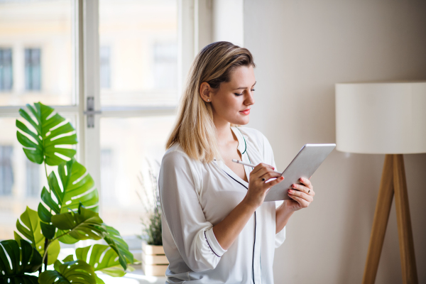 Young woman with tablet standing indoors in home office, working.