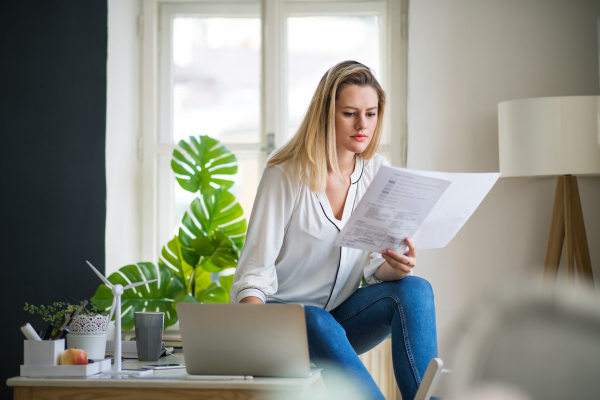 A young woman architect sitting at the desk indoors in home office, working.