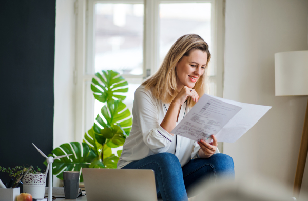 Young woman architect sitting on desk indoors in home office, working.