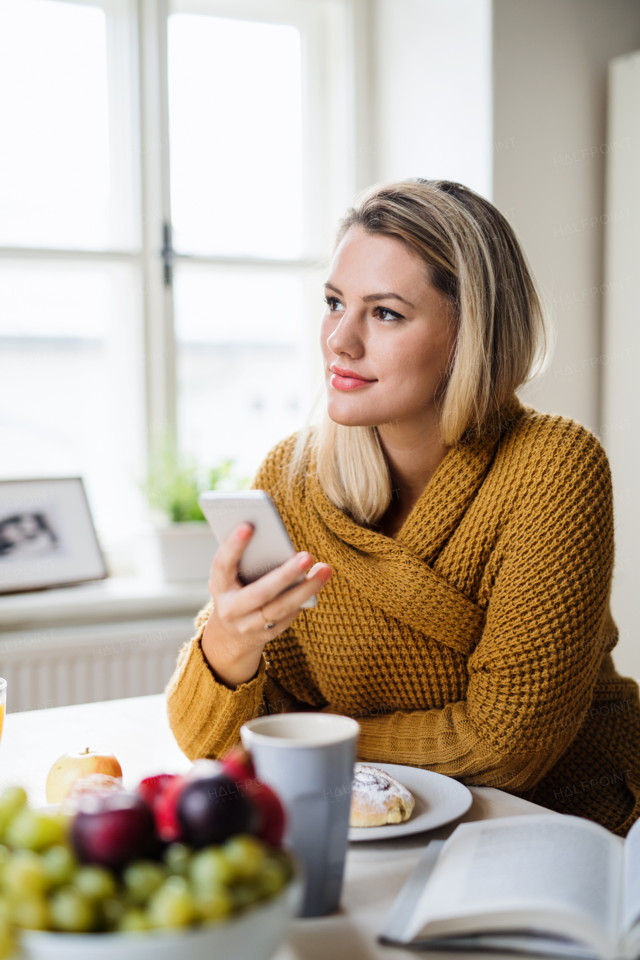 Young woman sitting at the table indoors at home, using smartphone when relaxing.