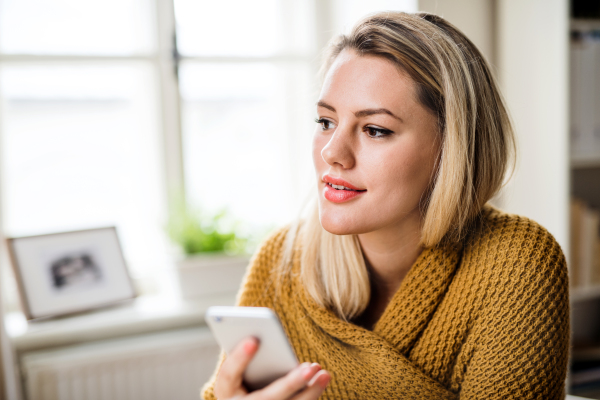 A young woman with smartphone indoors at home, relaxing.