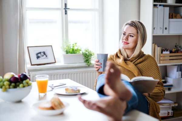 Happy young woman sitting at the table indoors at home, reading a book.