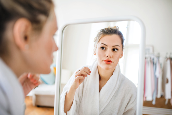 A young woman indoors at home in the morning, looking in mirror.