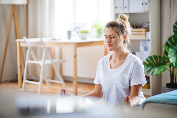 A young woman doing yoga exercise indoors at home, meditating.