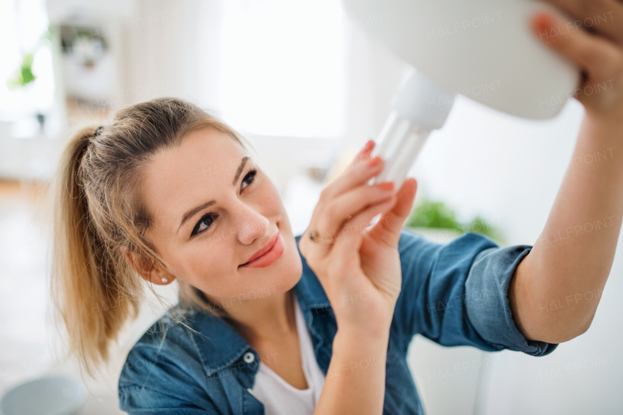 Happy young woman indoors at home, changing light bulb.