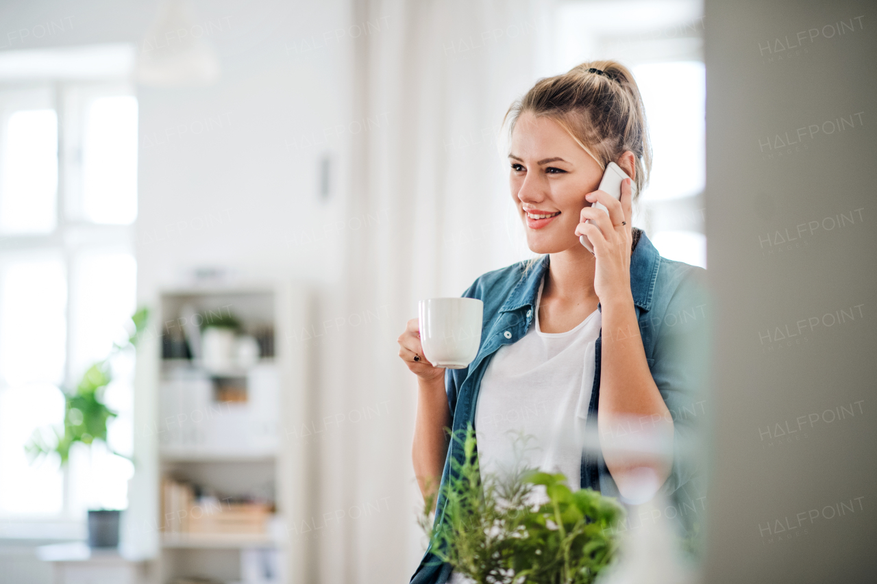 Relaxed young woman with smartphone indoors at home, enjoying a cup of coffee.