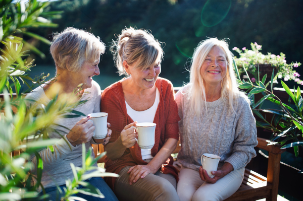 Group of senior women friends with coffee sitting outdoors on terrace, resting.