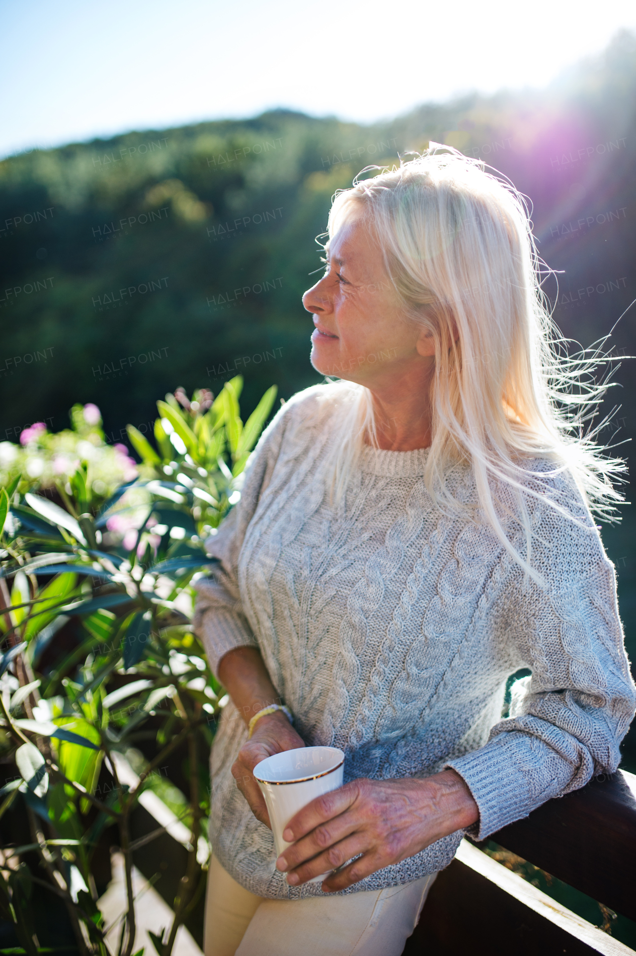 Side view of senior woman with coffee standing outdoors on terrace, resting.