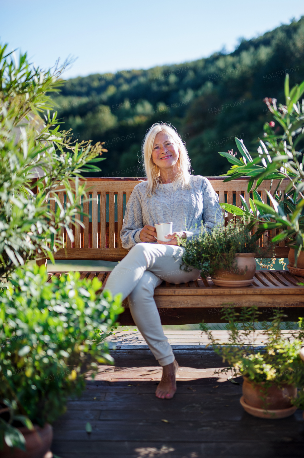 Front view of senior woman with coffee sitting outdoors on terrace, resting.