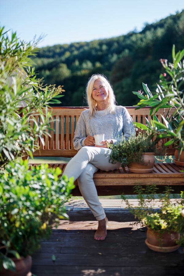 Front view of senior woman with coffee sitting outdoors on terrace, resting.