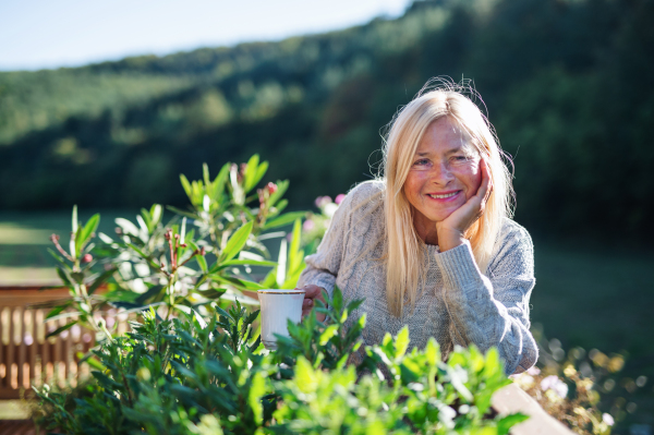 Front view of senior woman with coffee standing outdoors on terrace, resting.