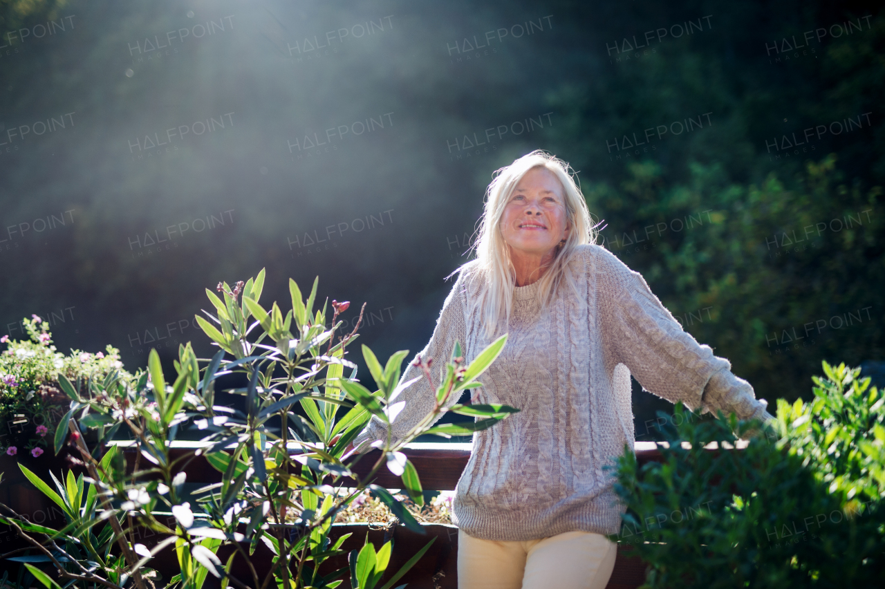 Front view of senior woman standing outdoors on terrace, resting.