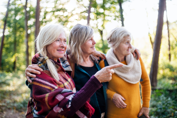 Senior women friends with hat walking outdoors in forest, talking.