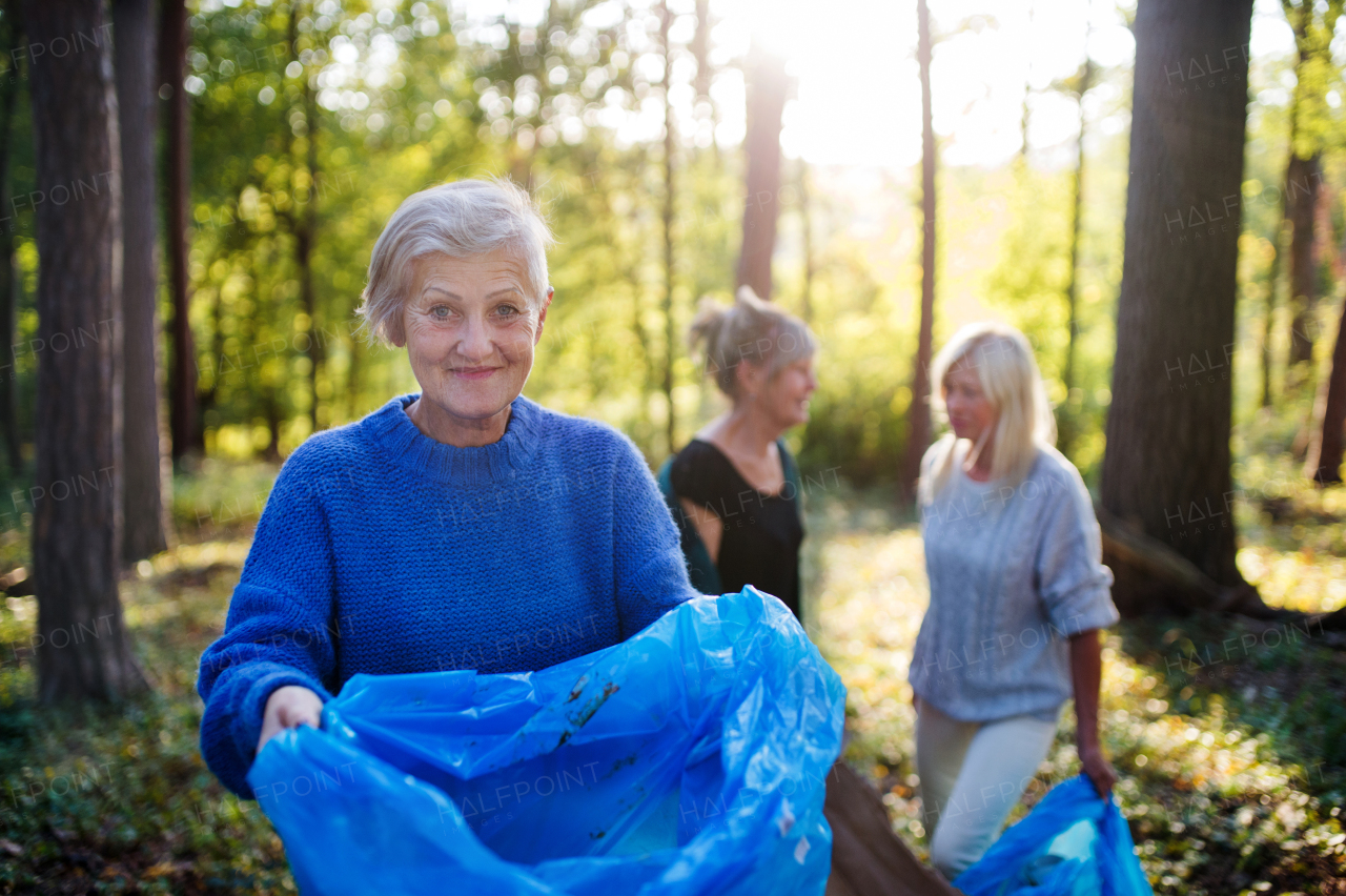 Group of senior women friends picking up litter outdoors in forest, a plogging concept.